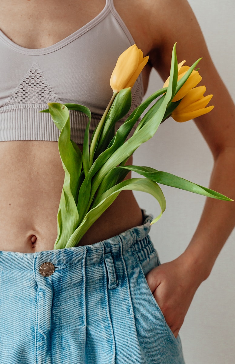 woman in blue denim shorts holding yellow flower